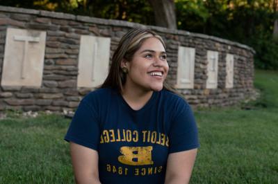 A student in Beloit gear sits in front of the Beloit College sign at the southwest side of campus...